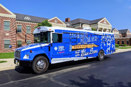 Photo of the Big Blue Bus, a school bus converted into a mobile food truck wrapped in a royal blue design, in front of Washington High School.